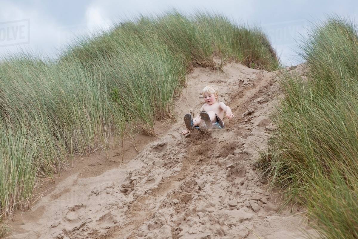 Boy sliding down sand dune Stock Photo Dissolve