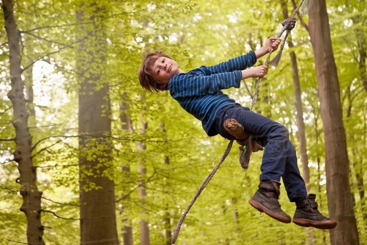 Boy swinging on rope in forest Stock Photo Dissolve