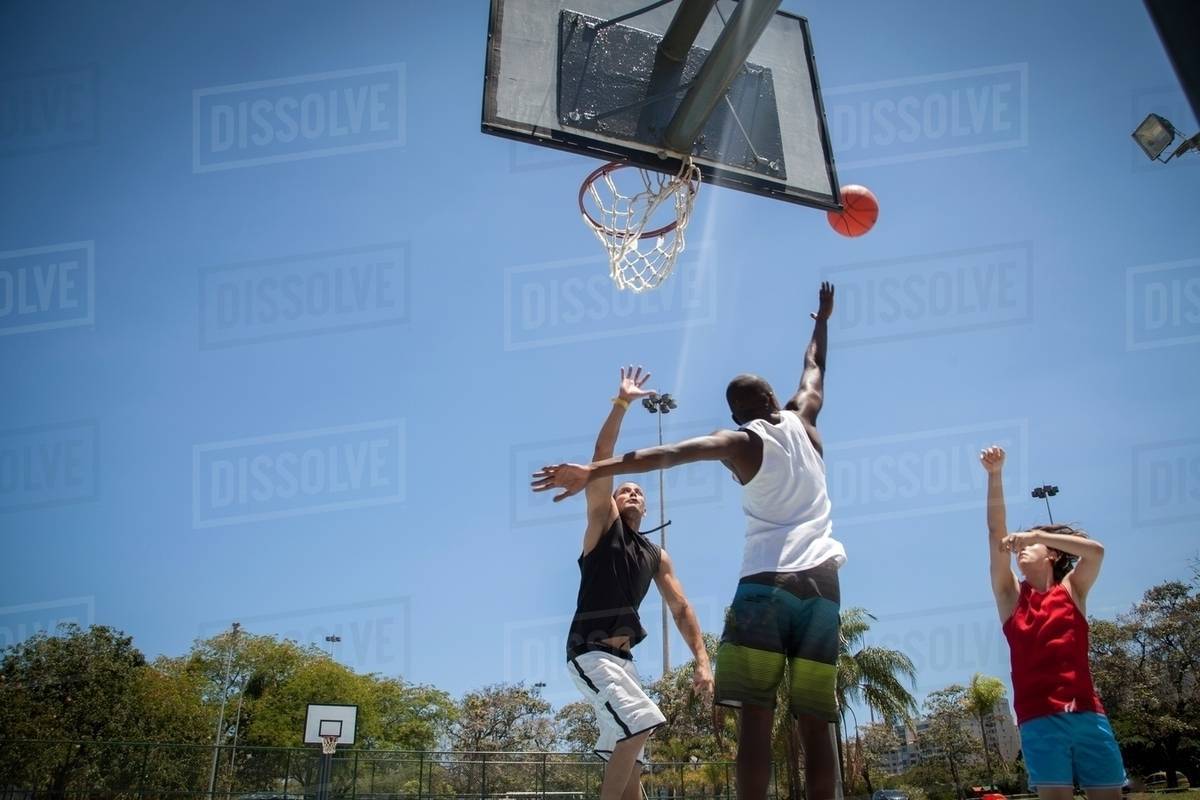 Male basketball players throwing ball toward basketball hoop Stock
