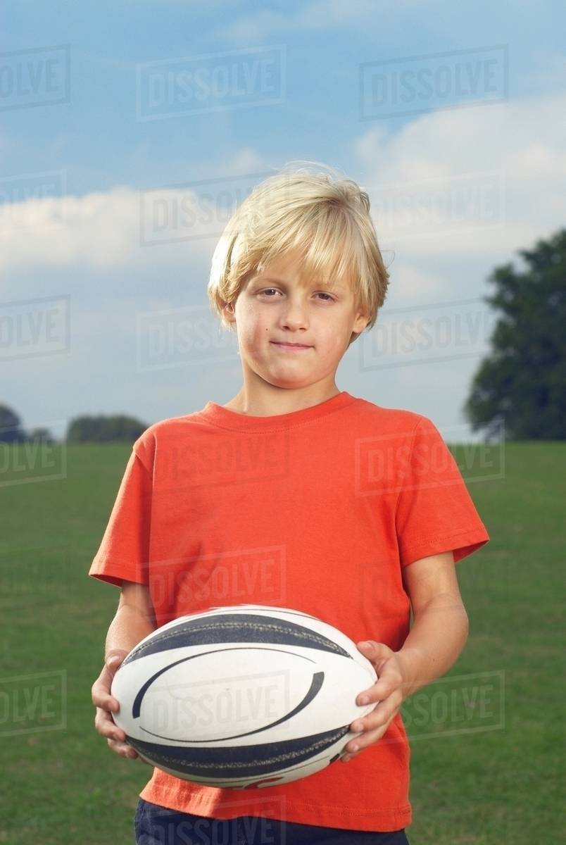 Boy holding rugby ball in filed Stock Photo Dissolve