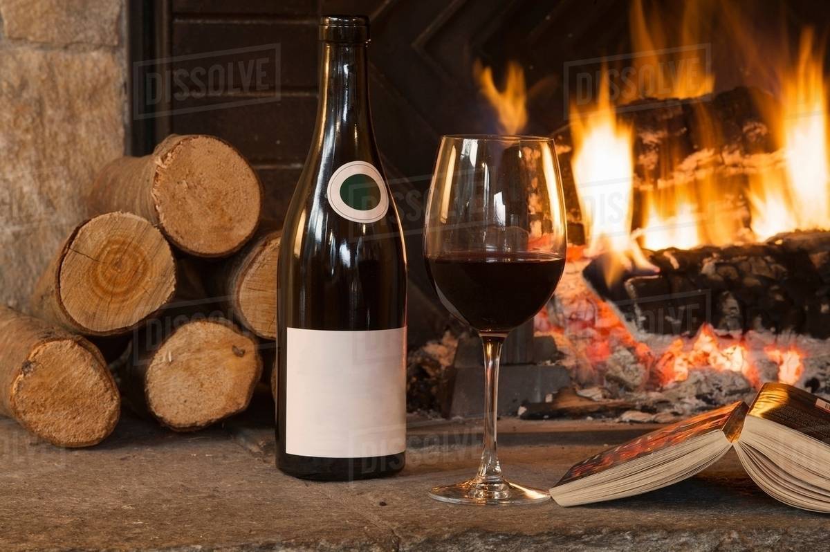 Glass of wine and book by fireplace Stock Photo Dissolve