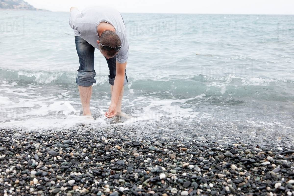 Man collecting pebbles on rocky beach - Stock Photo - Dissolve