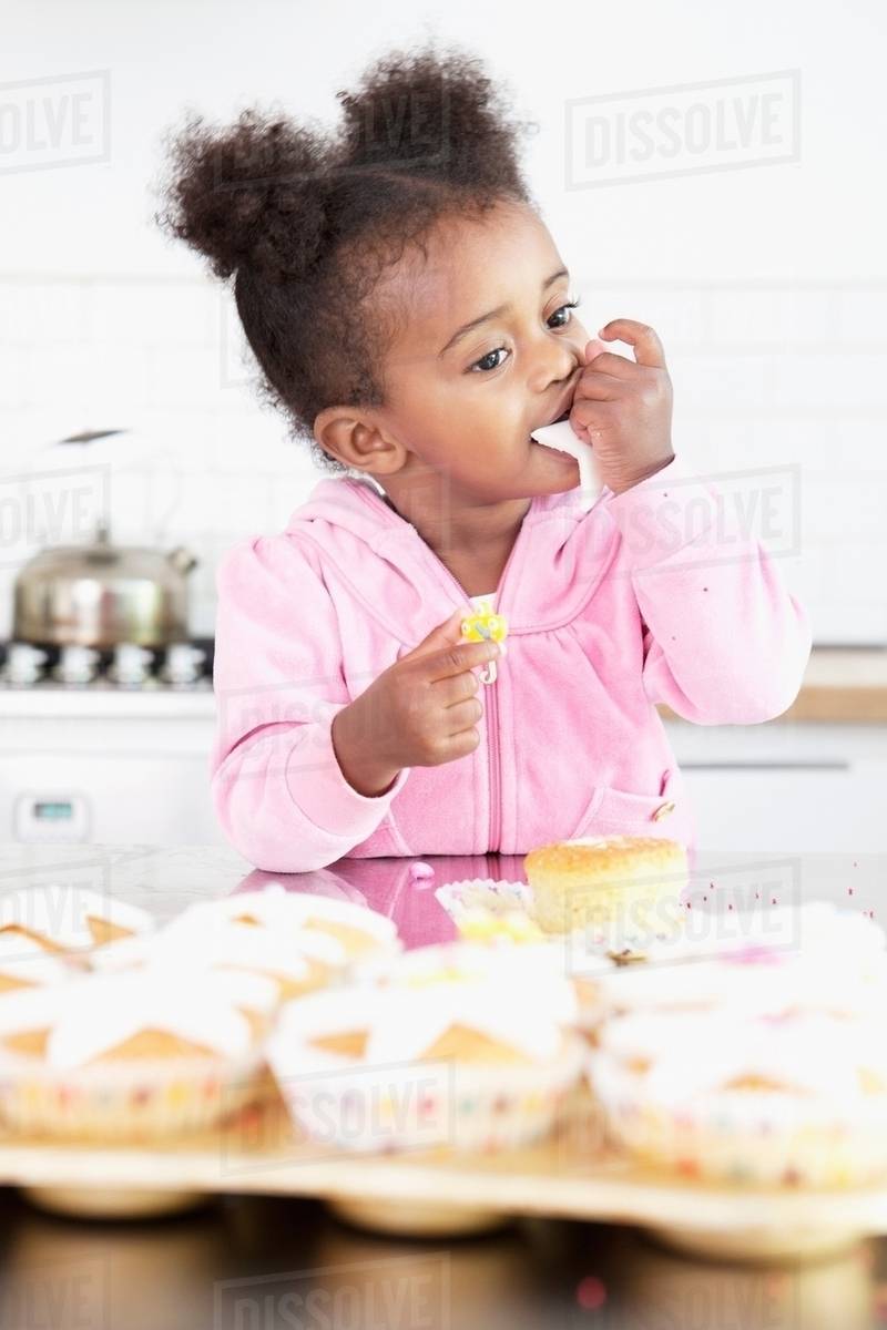 Girl eating cupcake frosting in kitchen Stock Photo Dissolve