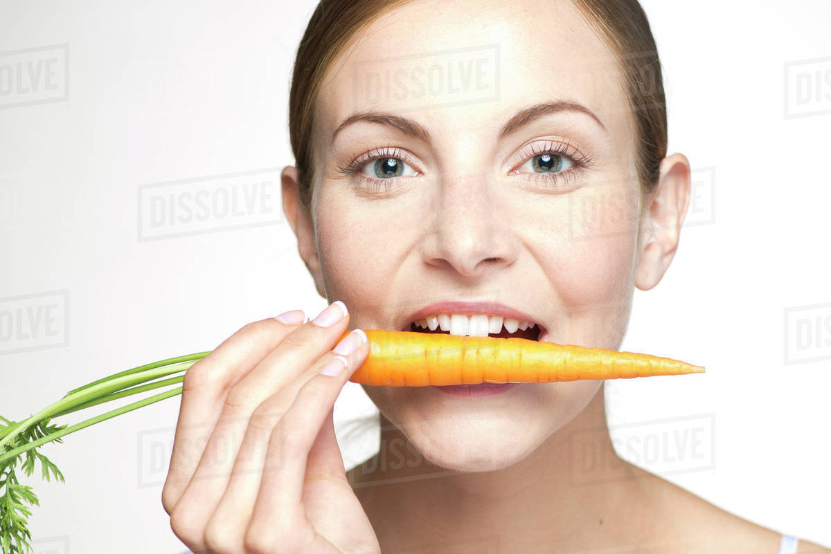 Young woman biting into carrot, portrait Stock Photo Dissolve
