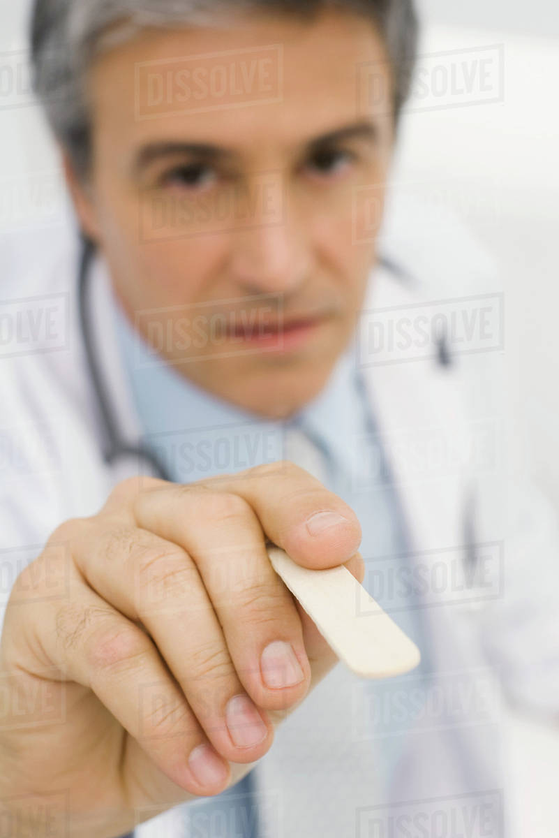 Doctor holding tongue depressor toward camera, closeup Stock Photo