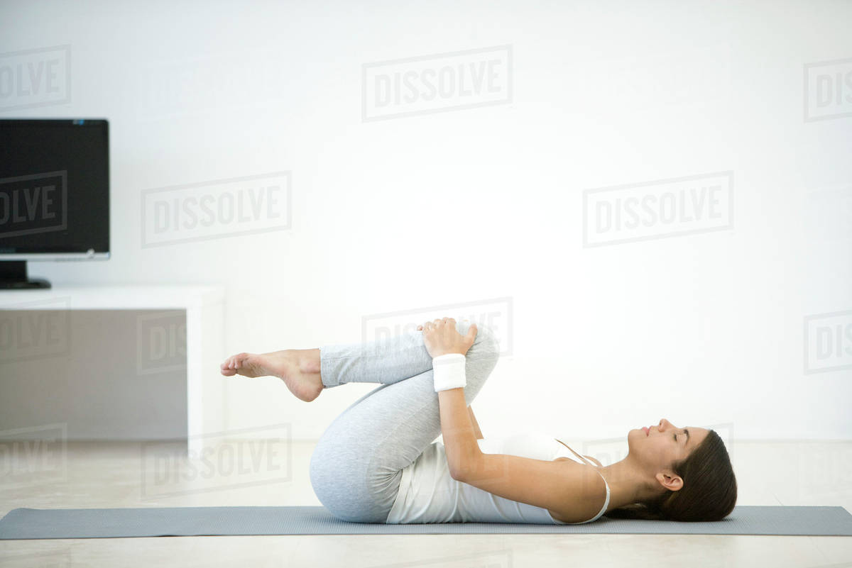 Woman lying on back, pulling knees up toward chest Stock Photo Dissolve
