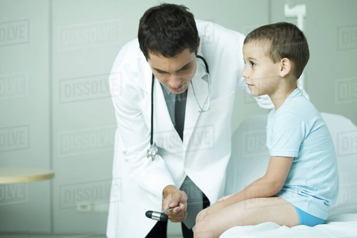 Doctor checking boy's reflexes with reflex hammer Stock Photo Dissolve