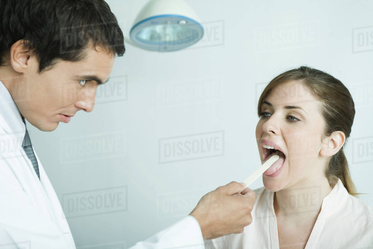 Doctor holding down woman's tongue with tongue depressor Stock Photo