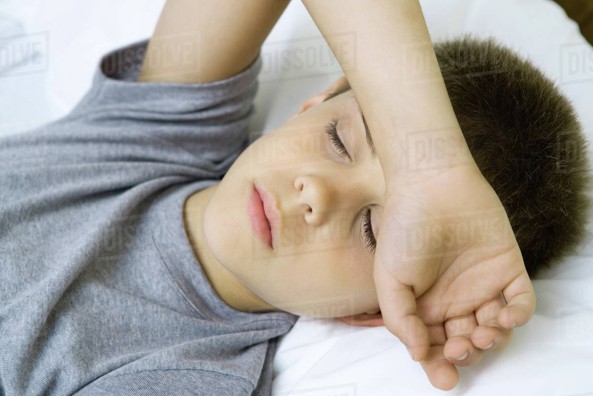 Boy lying down with arm covering forehead Stock Photo Dissolve