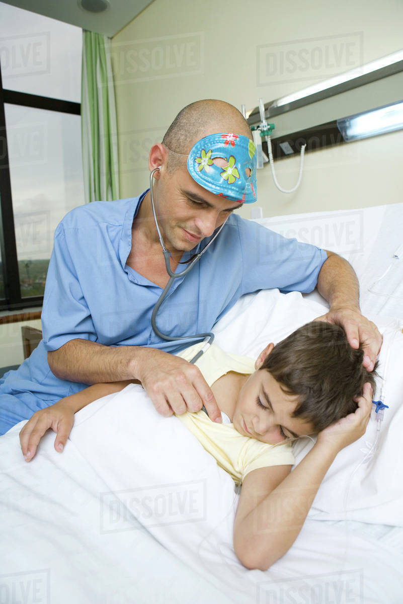 Boy lying in hospital bed, sleeping, doctor holding stethoscope to boy
