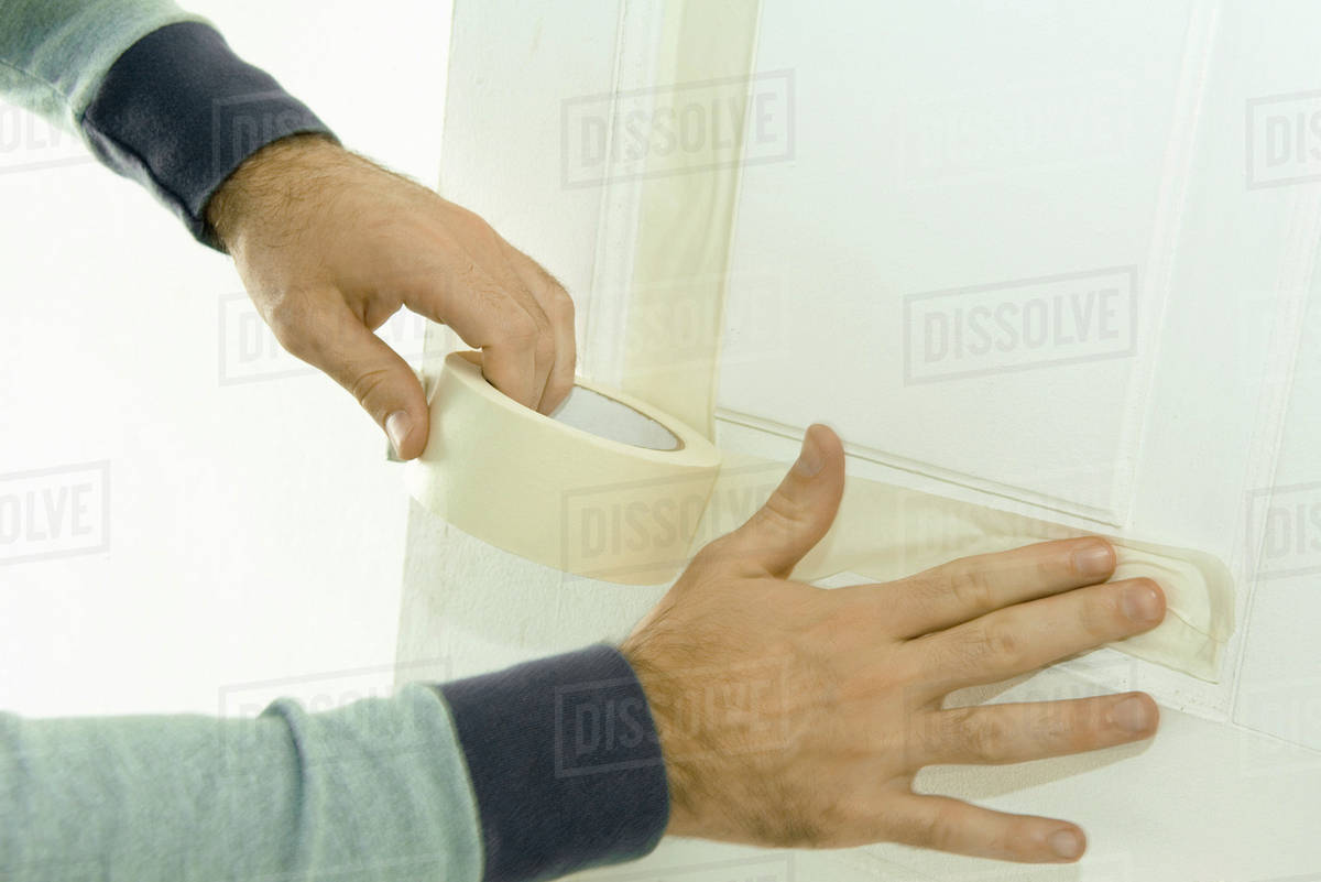 Man putting masking tape on door woodwork, closeup of hands Stock Photo Dissolve