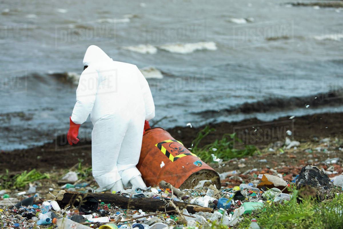 Person in protective suit carrying barrel of hazardous waste on