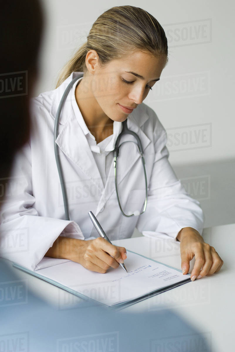 Doctor writing at desk, patient in foreground Stock Photo Dissolve