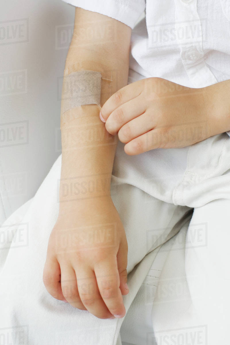 Little boy picking at adhesive bandage on his arm, cropped view Stock