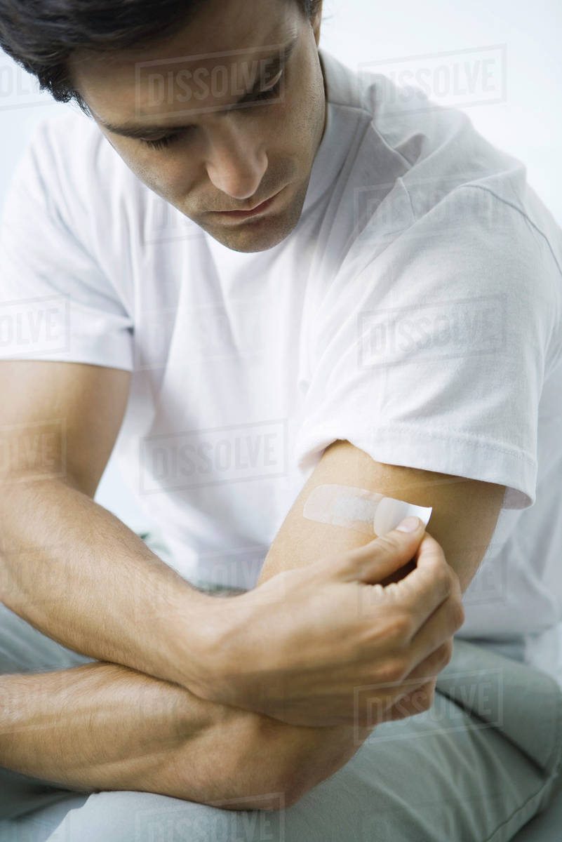 Man putting adhesive bandage on his arm Stock Photo Dissolve
