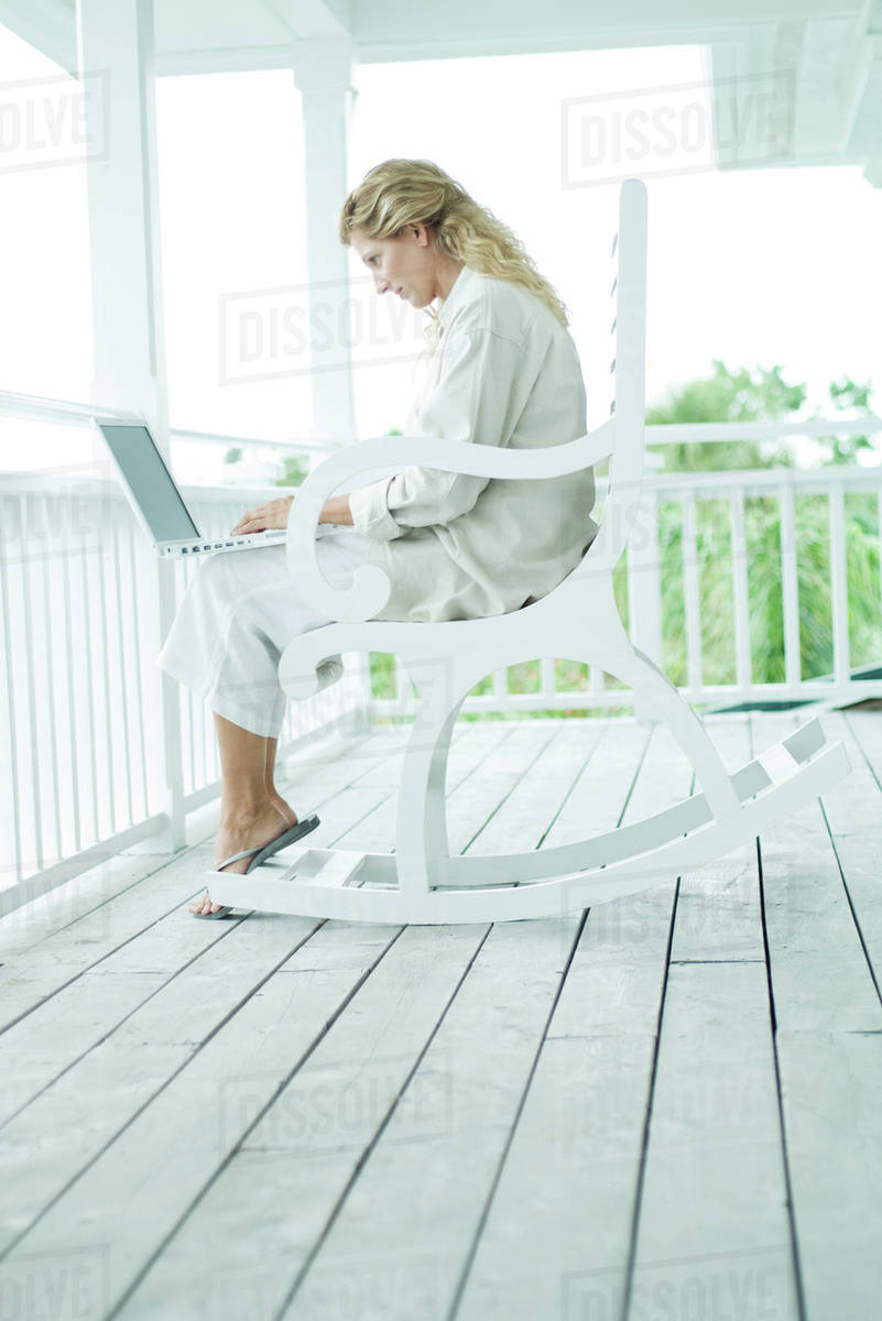 Woman sitting in rocking chair on porch, using laptop computer, full ...