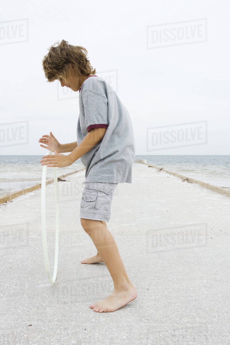 Boy standing on pier, playing with plastic hoop, side view, full length Royalty-free stock photo