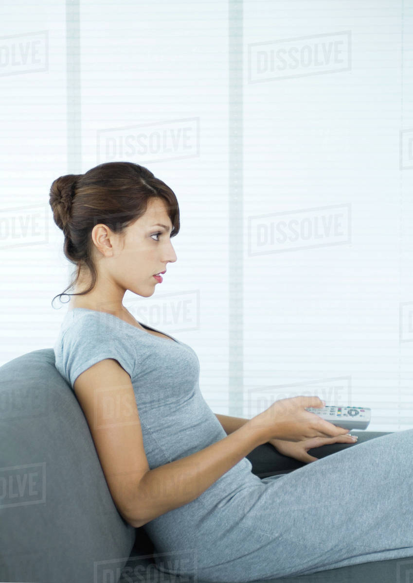 Woman Sitting On Sofa Pointing Remote Control Side View Stock