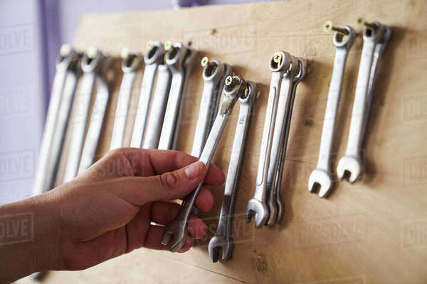 Close-up shot of hand taking a combination spanner from a wall rack ...