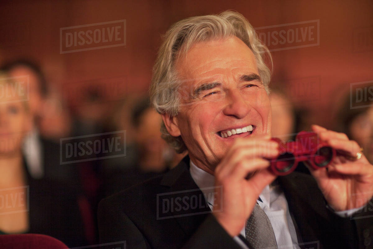 Man with opera glasses laughing in theater audience Stock Photo