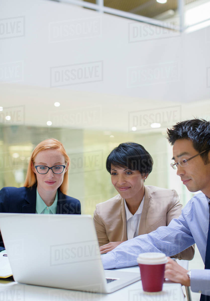Business people gathered around laptop in office building cafe ...