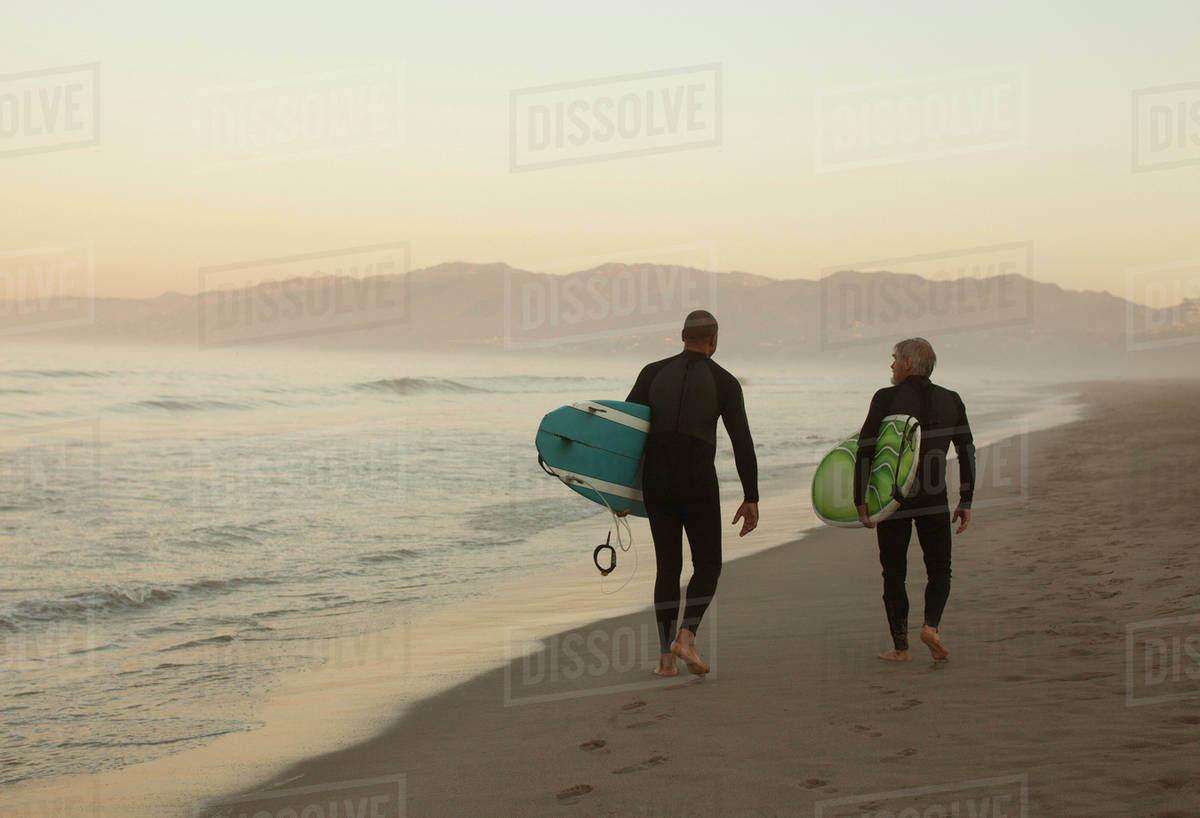 Older surfers carrying boards on beach Stock Photo Dissolve