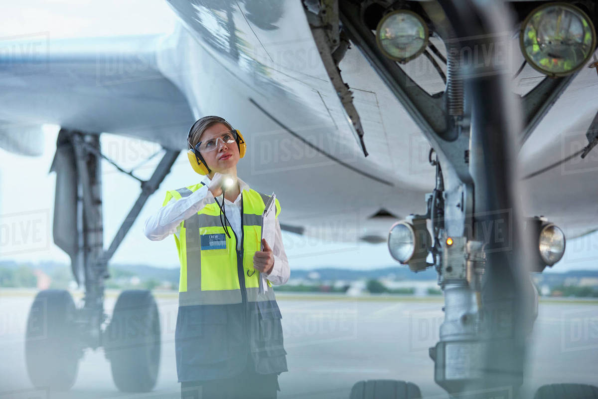 Ground crew worker under airplane with flashlight on airport tarmac