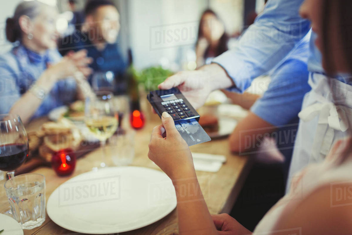 Woman with credit card paying waiter, using credit card reader at