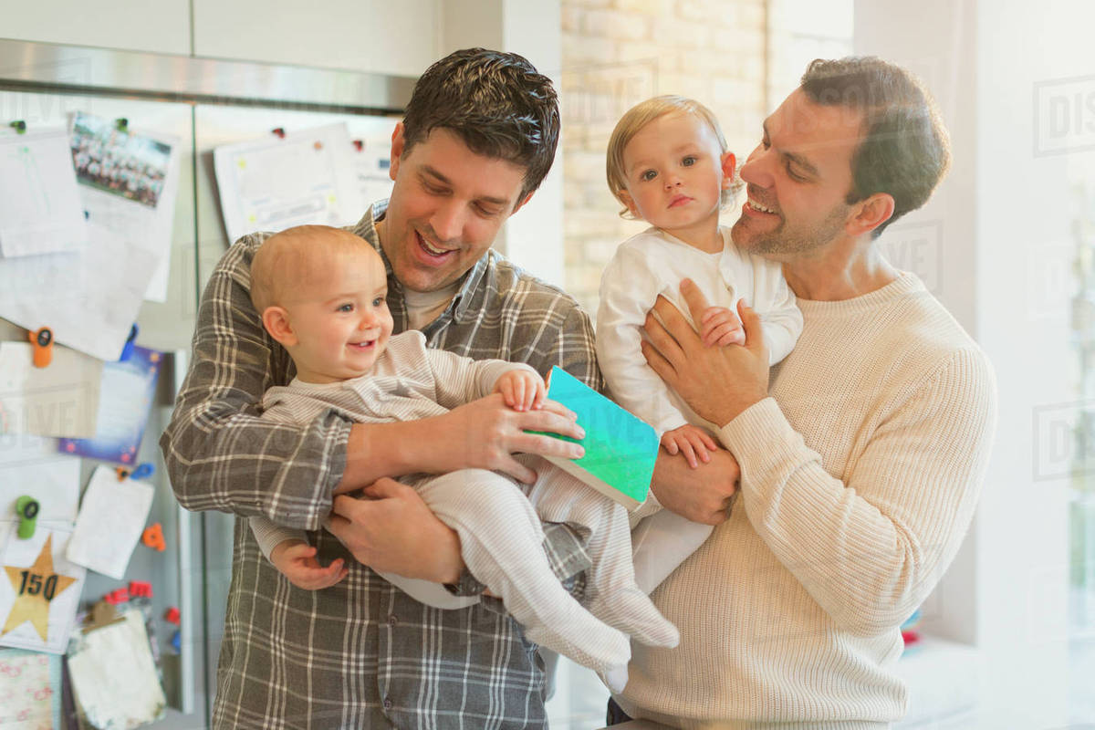 Male gay parents holding baby sons in kitchen Royalty-free stock photo