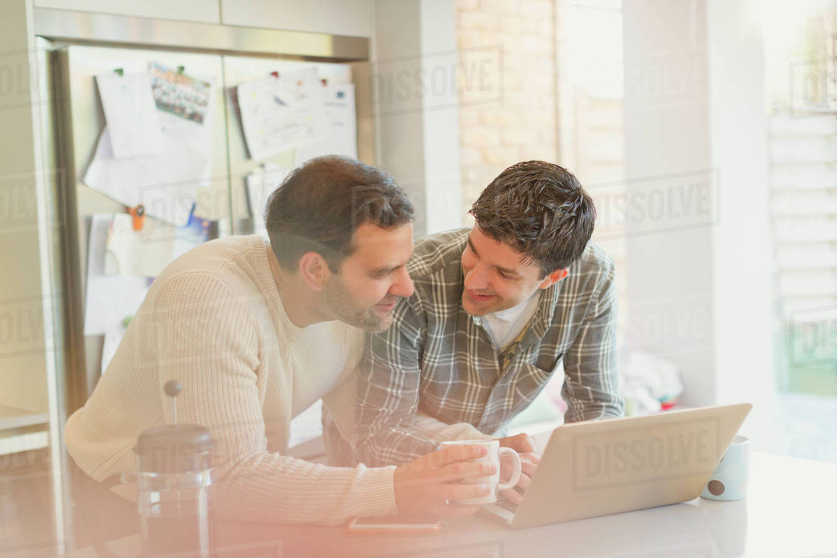 Male gay couple using laptop and drinking coffee in kitchen Royalty-free stock photo