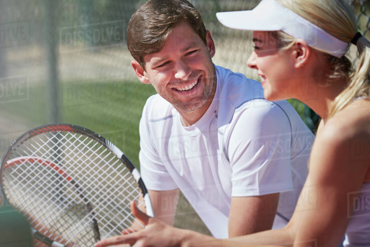 Smiling male and female tennis players resting and talking with tennis