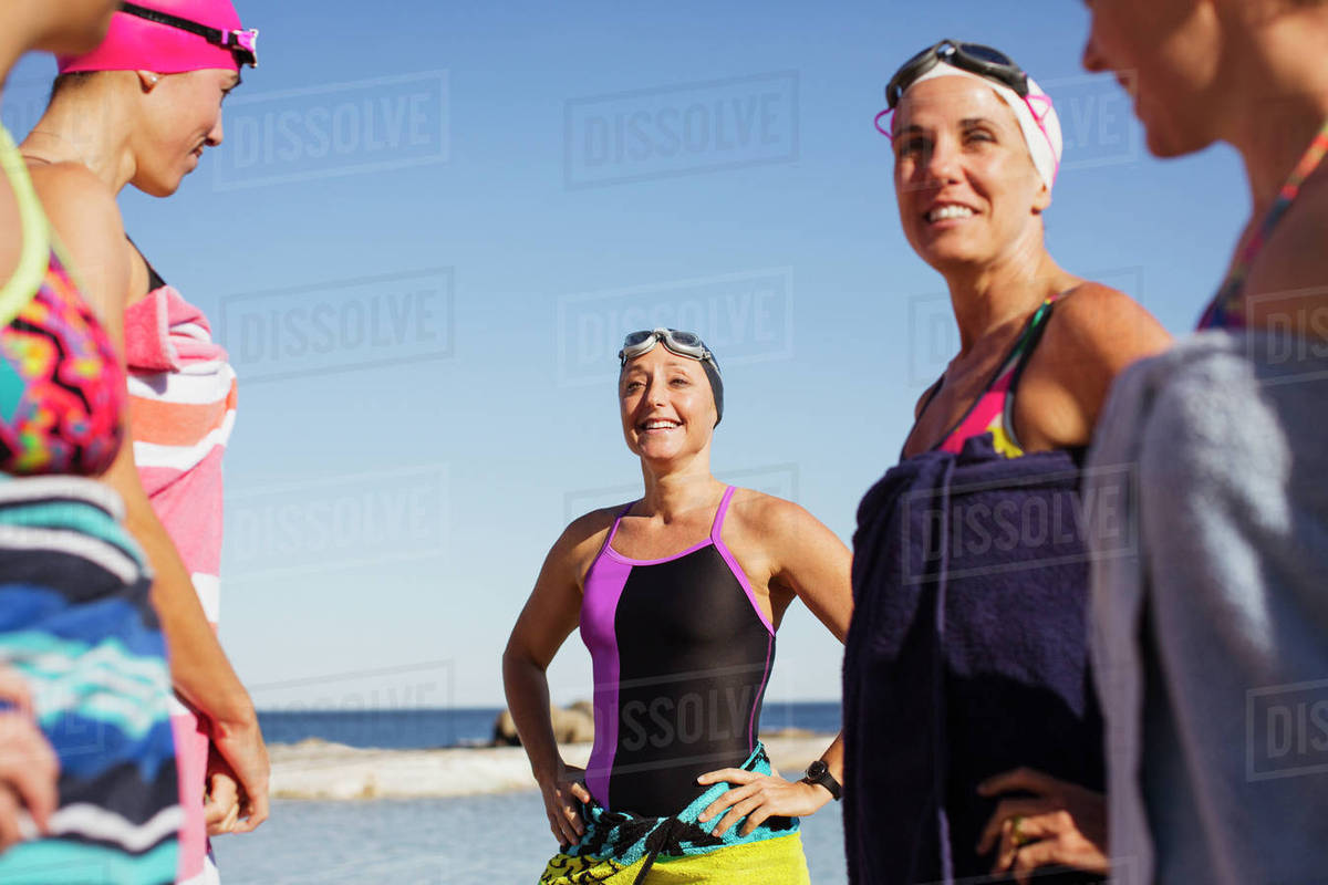 Smiling female open water swimmers wrapped din towels on sunny beach