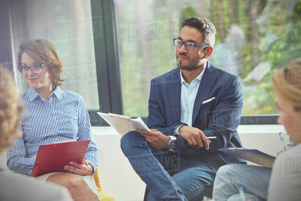 Attentive man with clipboard listening in group therapy session Stock