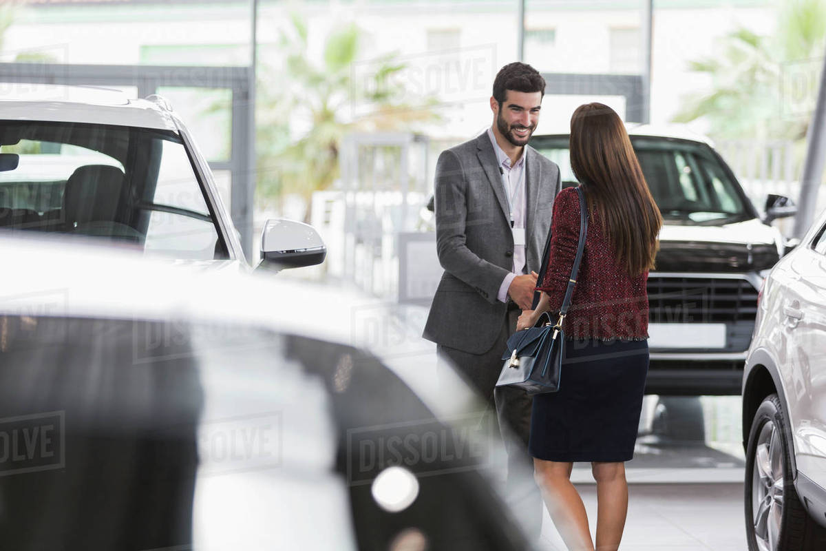 Car salesman greeting, shaking hands with female customer in car dealership showroom Stock