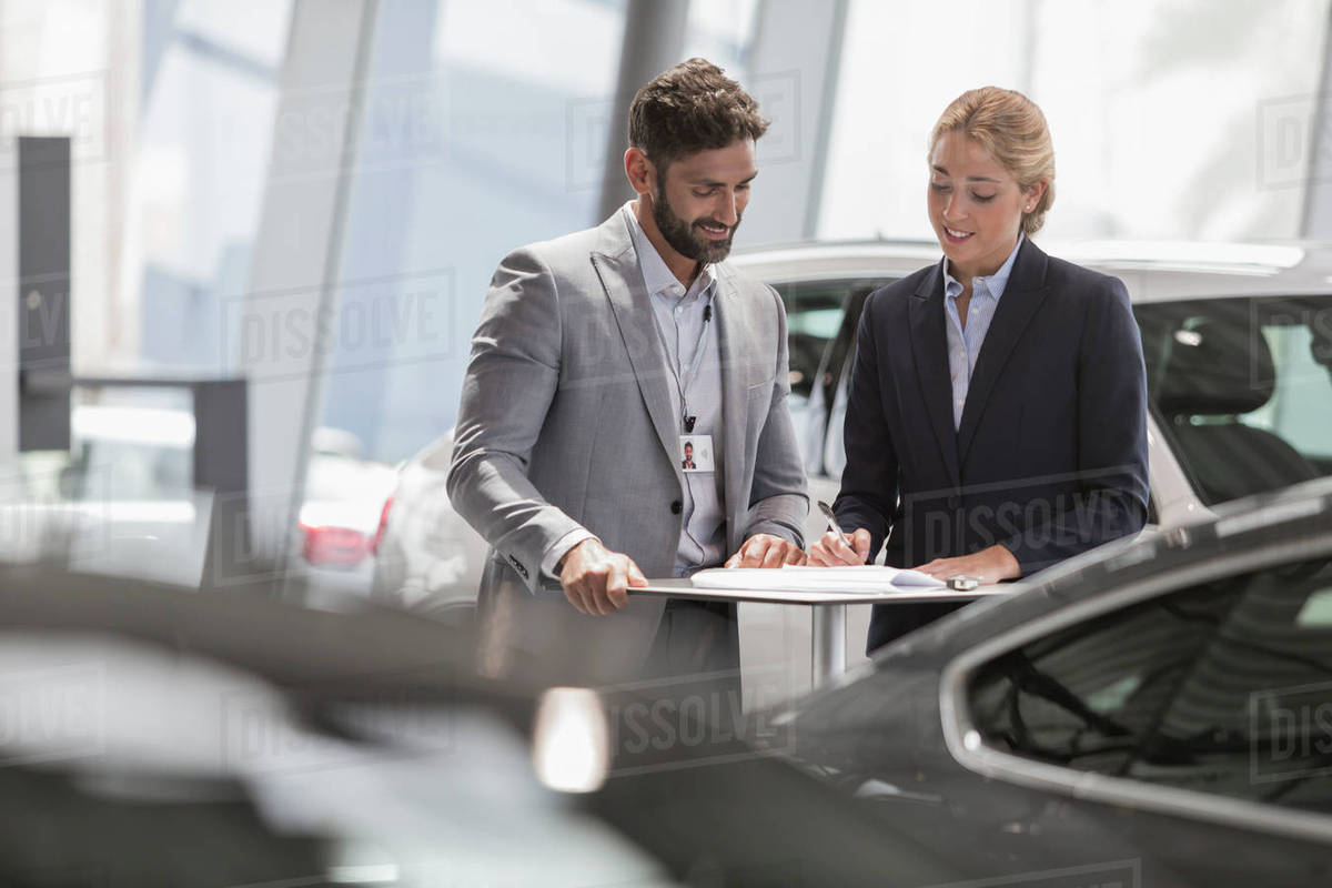 Car salesman and female customer reviewing financial contract paperwork