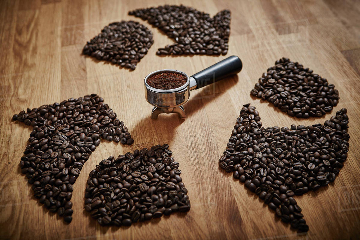 Coffee beans forming recycle symbol around espresso grounds in portafilter Stock Photo Dissolve