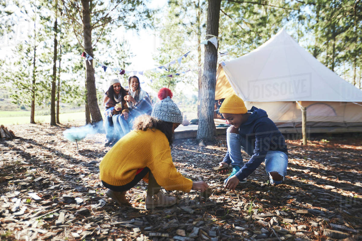 Brother and sister gathering kindling at sunny campsite in woods ...
