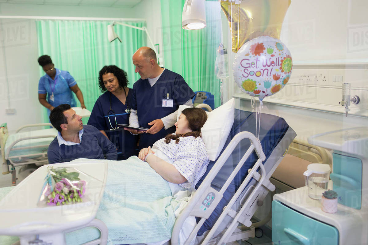 Doctors making rounds, talking with couple in hospital ward Stock