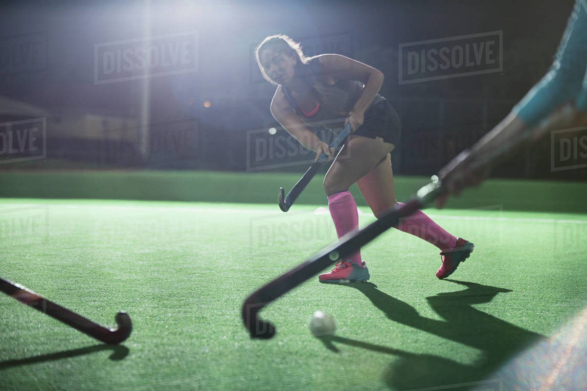 Young female field hockey running with hockey stick on field at night