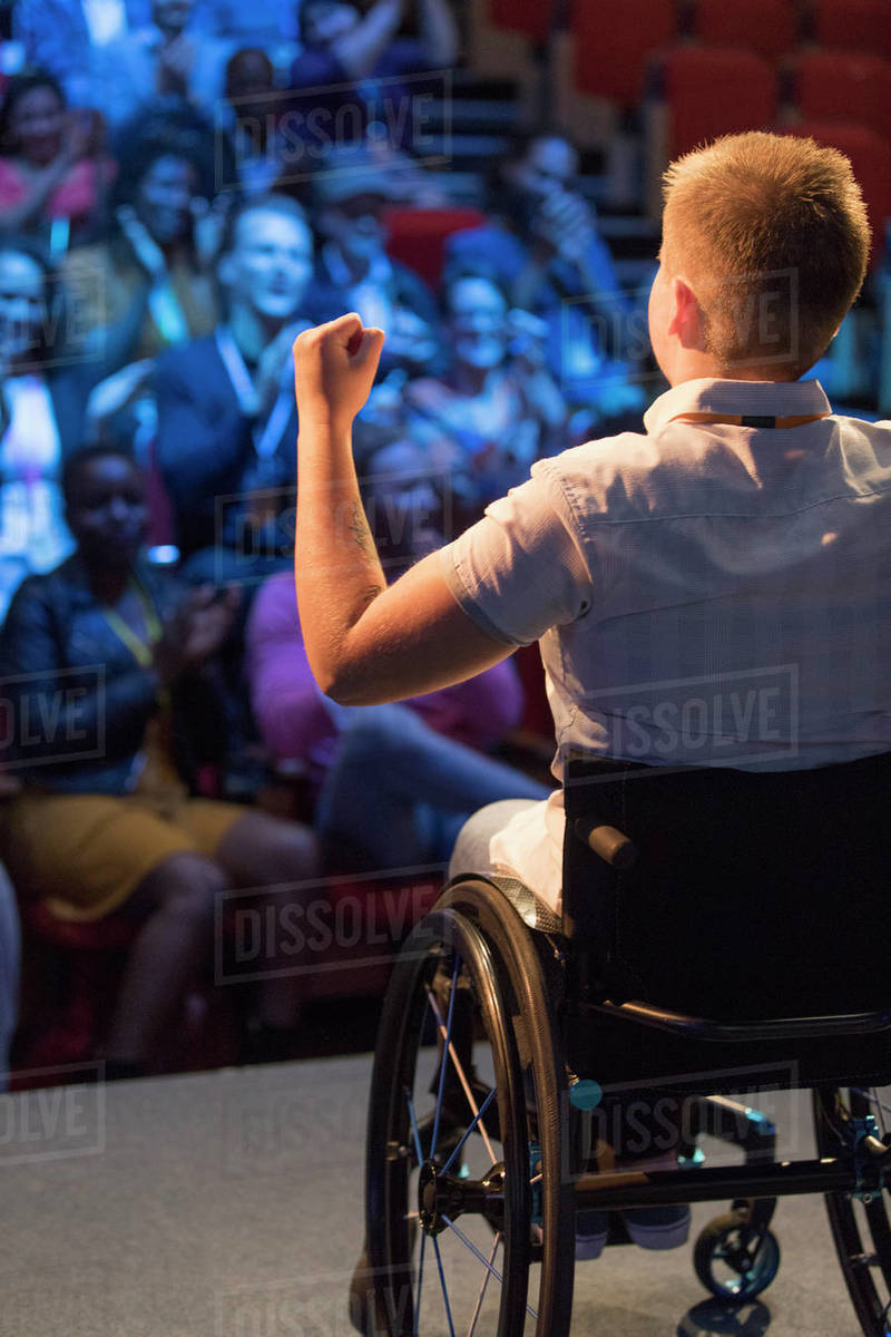 Female speaker in wheelchair gesturing on stage for cheering audience