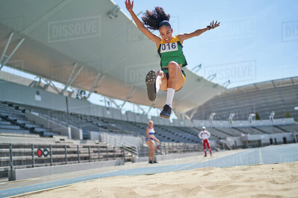 Female track and field athlete long jumping over sand Stock Photo