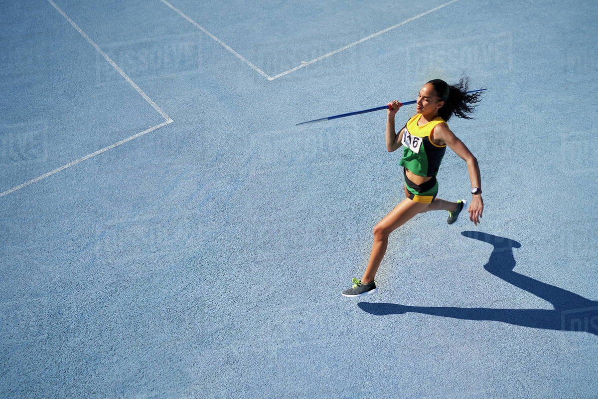 Female track and field athlete throwing javelin on sunny blue track