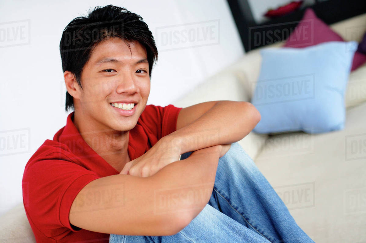 Man sitting on sofa, arms crossed, hugging knees, looking at camera