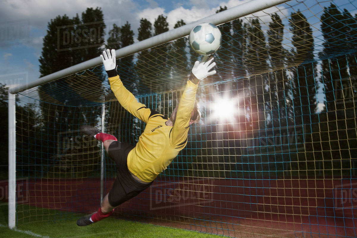 Full length of soccer goalkeeper diving to block ball Stock Photo
