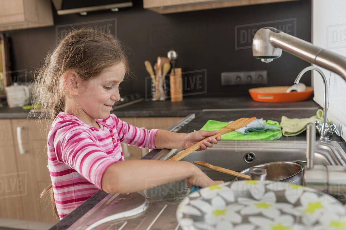 Smiling girl washing utensils in kitchen at home Stock Photo Dissolve