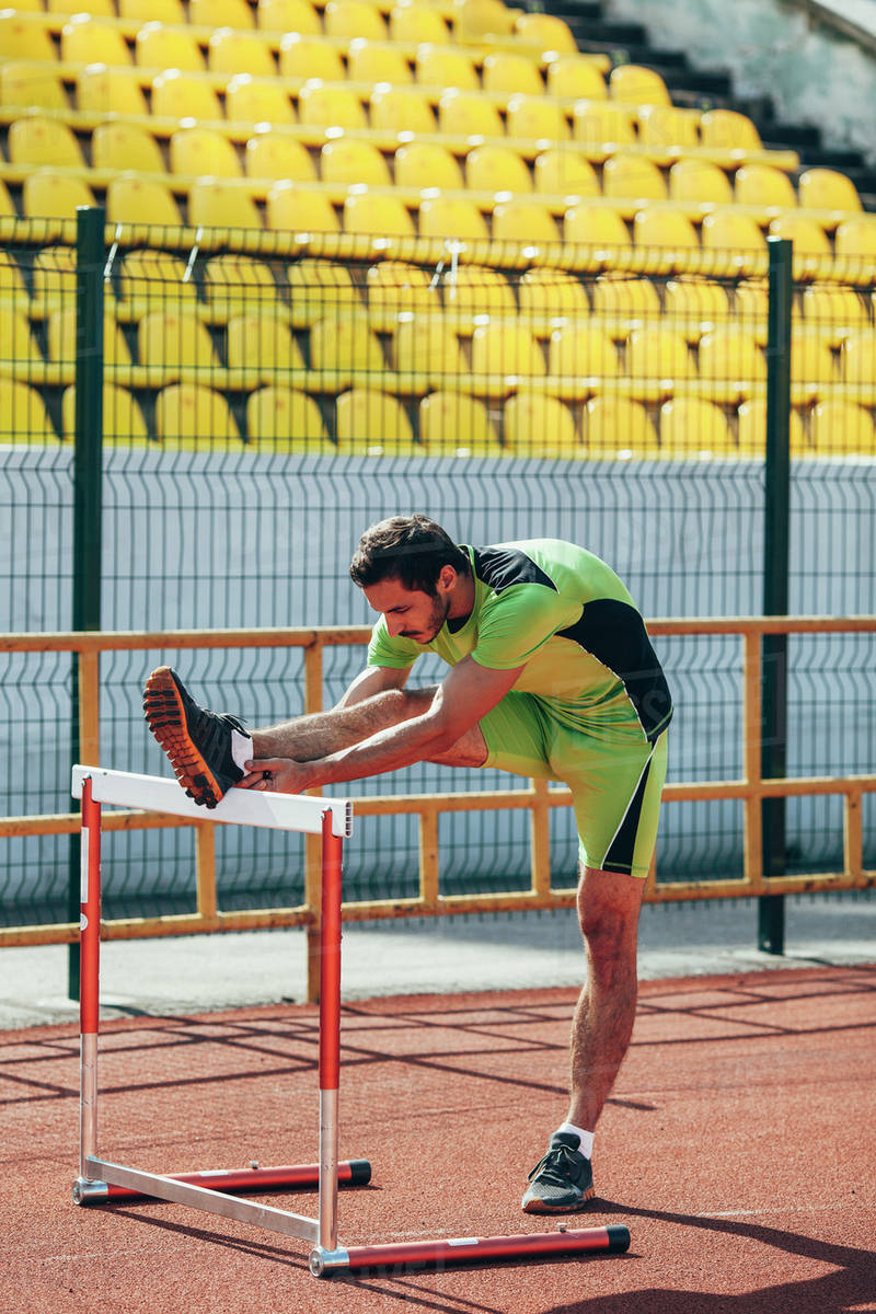 Full length of track and field athlete warming up on hurdle Stock