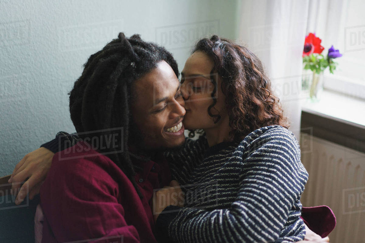 Woman kissing man on cheek while sitting on armchair at home Royalty-free stock photo