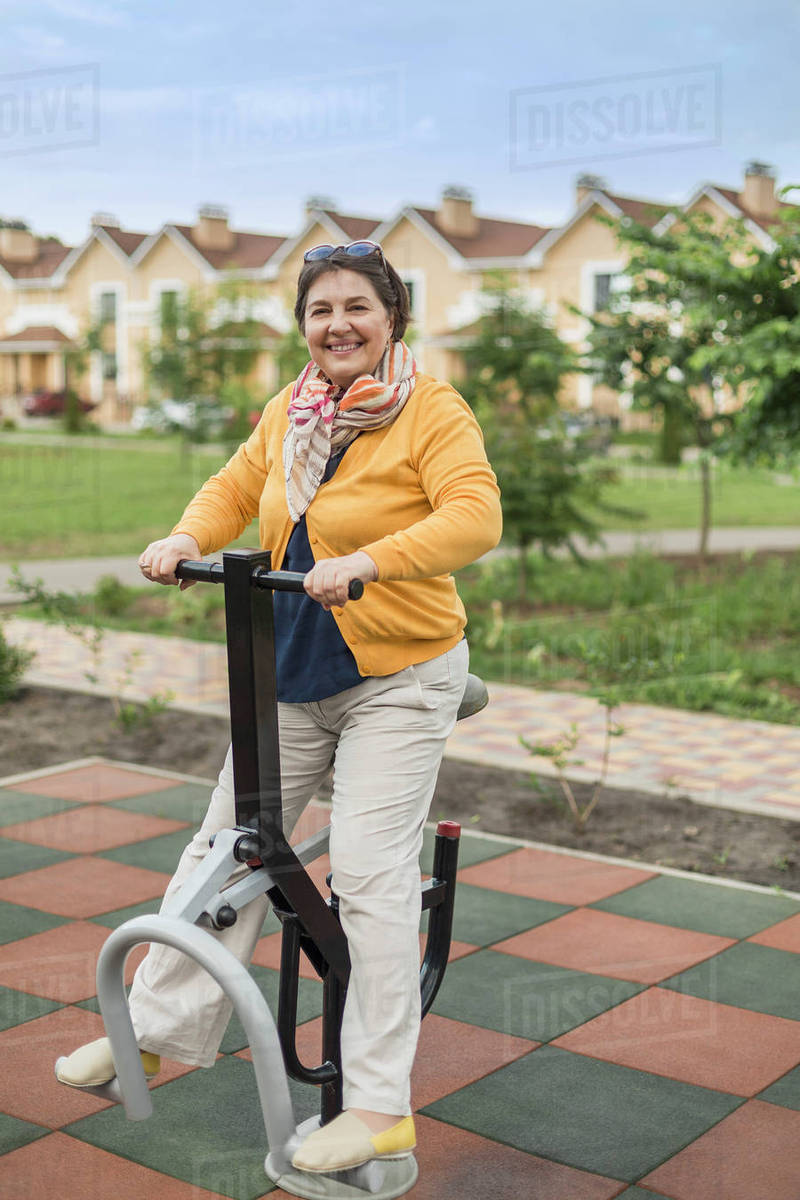Full length of smiling senior woman using exercise equipment at park ...