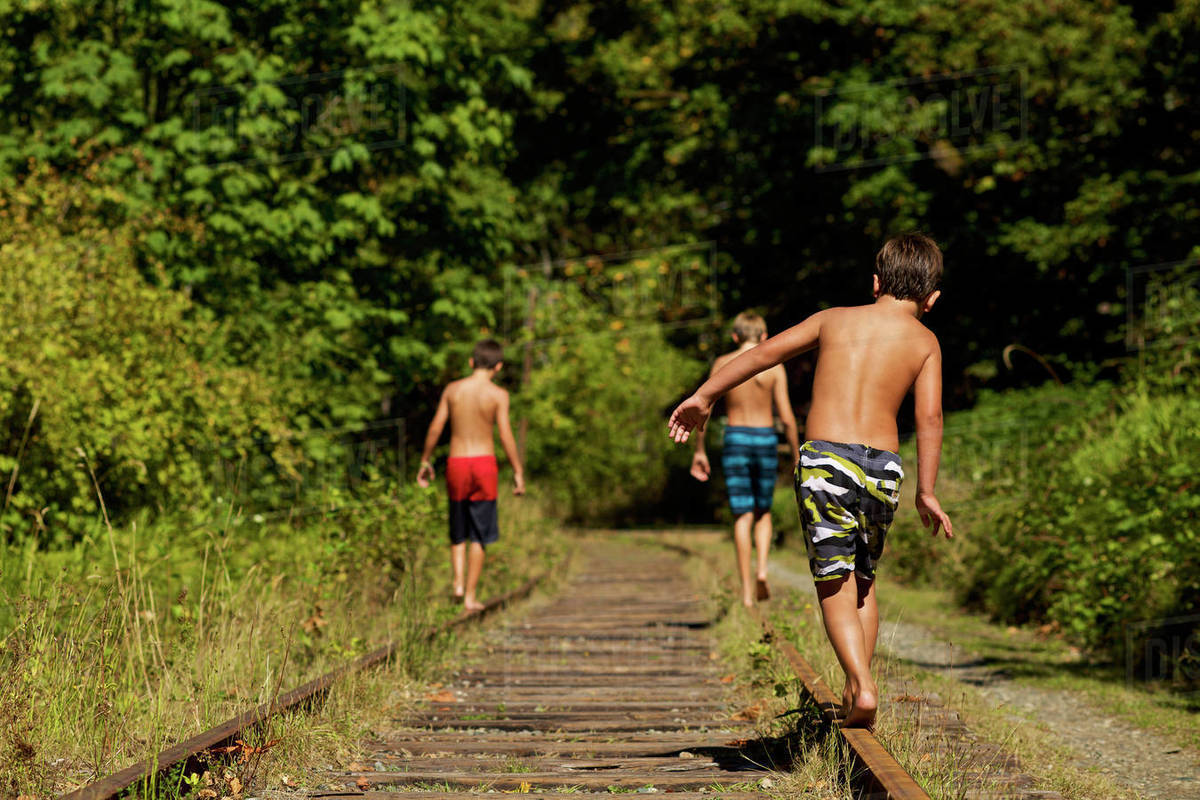 Boys in swim trunks walking along sunny railroad tracks in woods Royalty-free stock photo