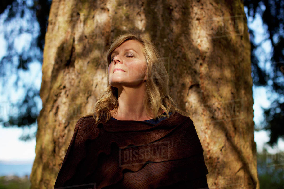 Portrait serene woman with eyes closed standing at sunny tree trunk Royalty-free stock photo